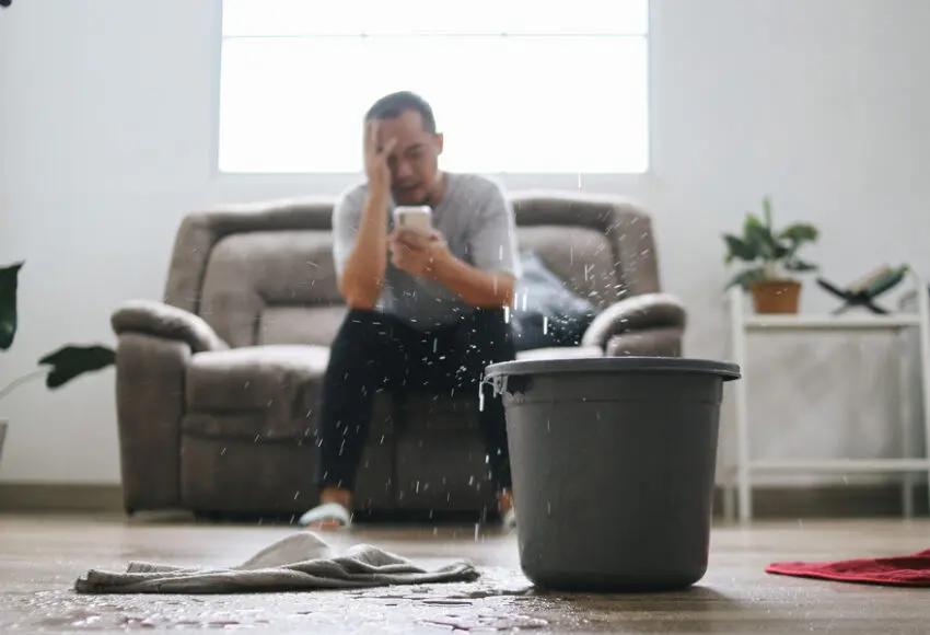 Stressed Man Calling Home Service to Repair Roof Leak at Home. A Bucket placed for Water From Leaks