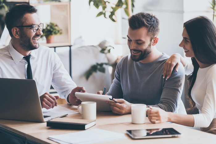 Pulic Adjuster with clients. Cheerful young man signing some documents while sitting together with his wife