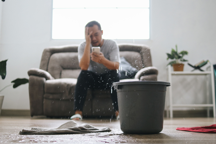 Stressed Man Calling Home Service to Repair Roof Leak at Home. A Bucket placed for Water From Leaks